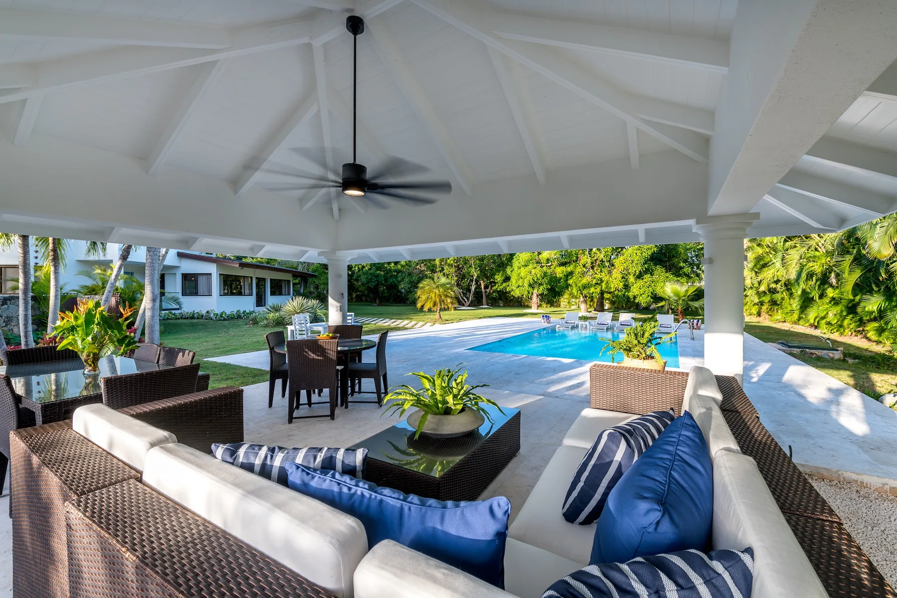 Una zona de estar exterior cubierta da a una piscina y un jardín.