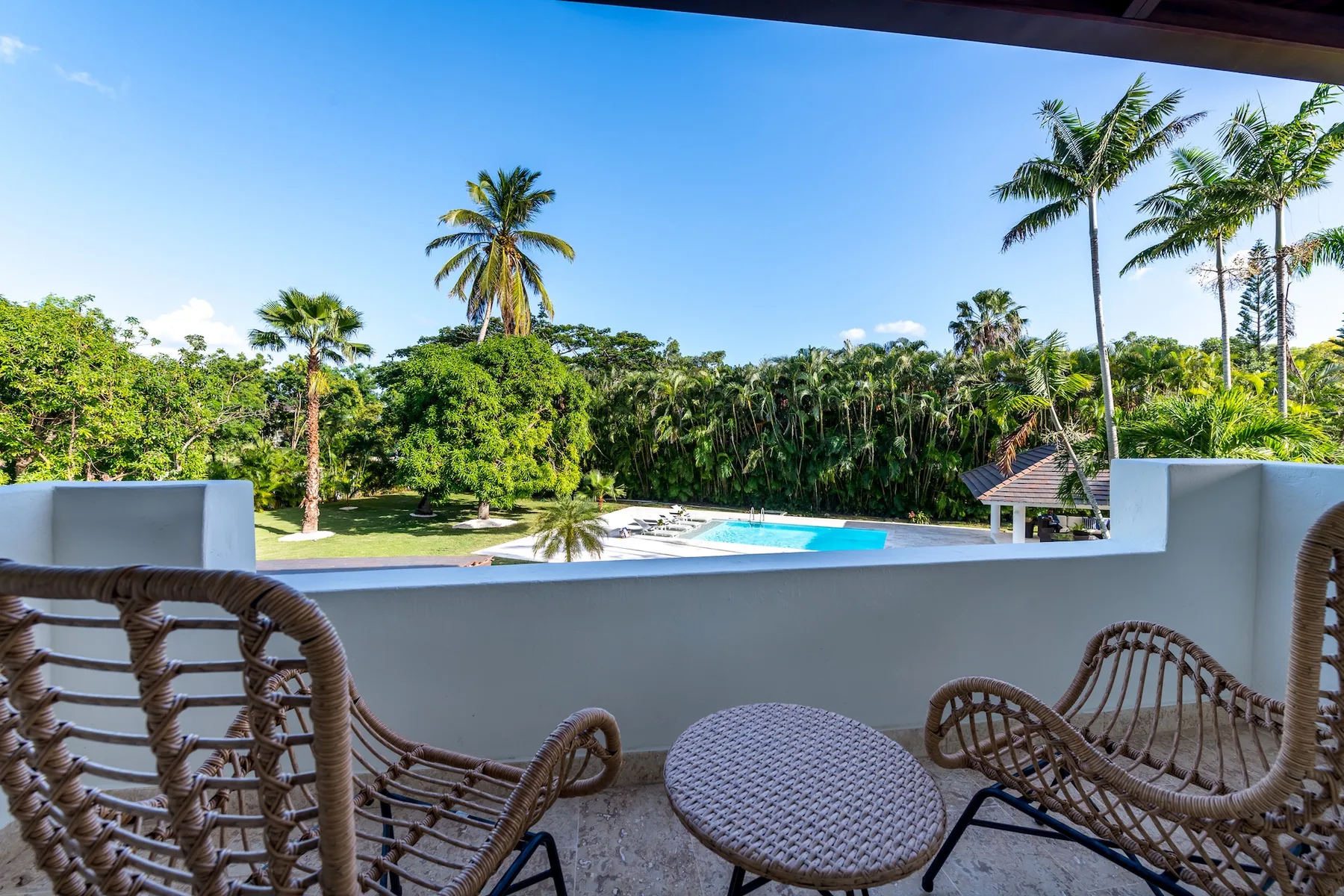 Una zona de estar en el balcón da a una piscina y vegetación tropical.
