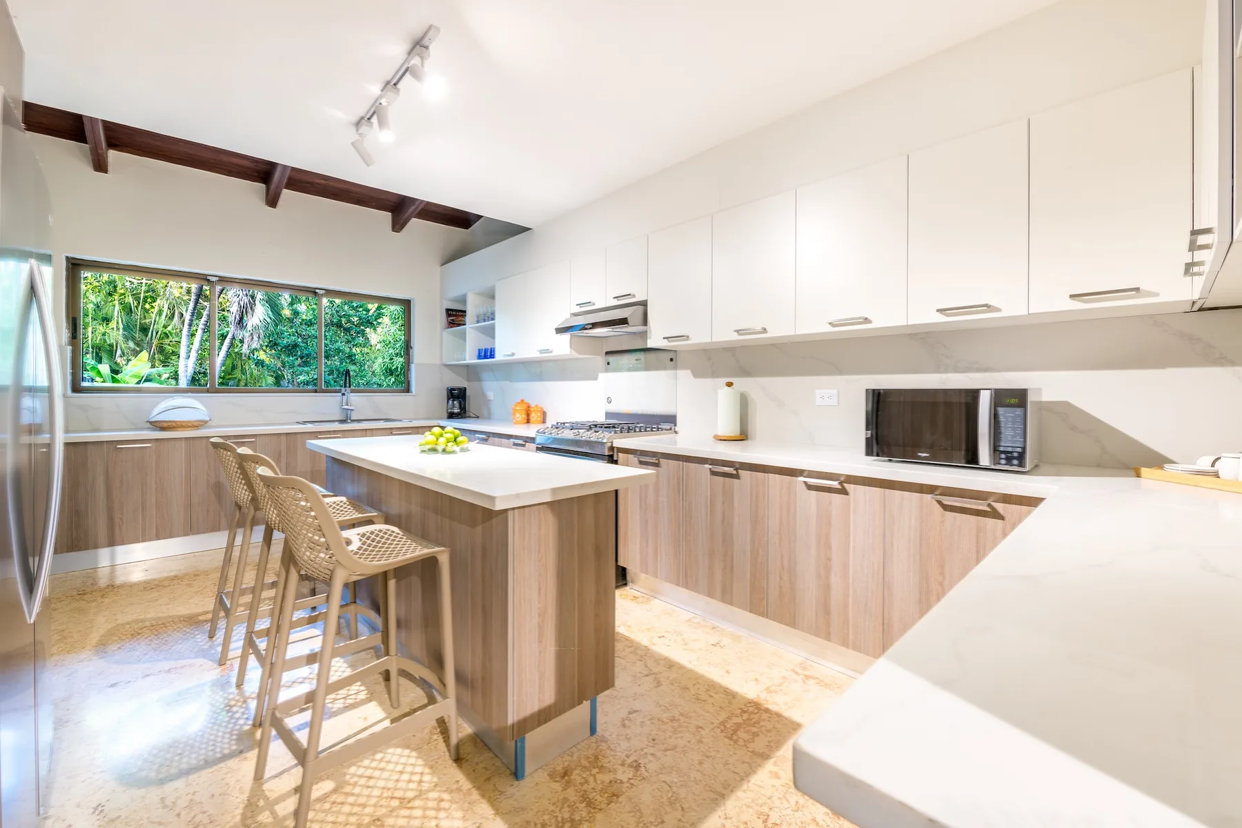 Una cocina moderna y luminosa con una isla central y ventanas que dan a la vegetación.