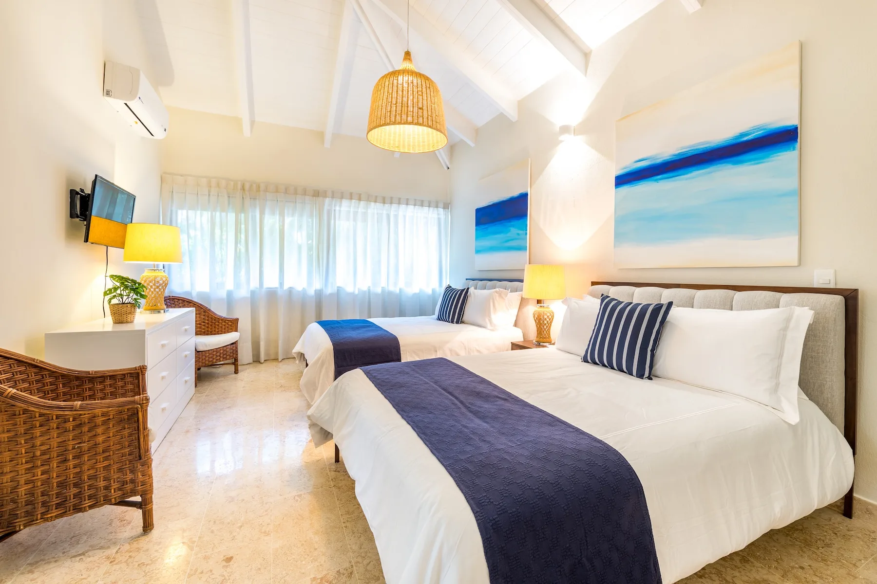 Un dormitorio luminoso con dos camas, ropa de cama blanca y detalles azules.
