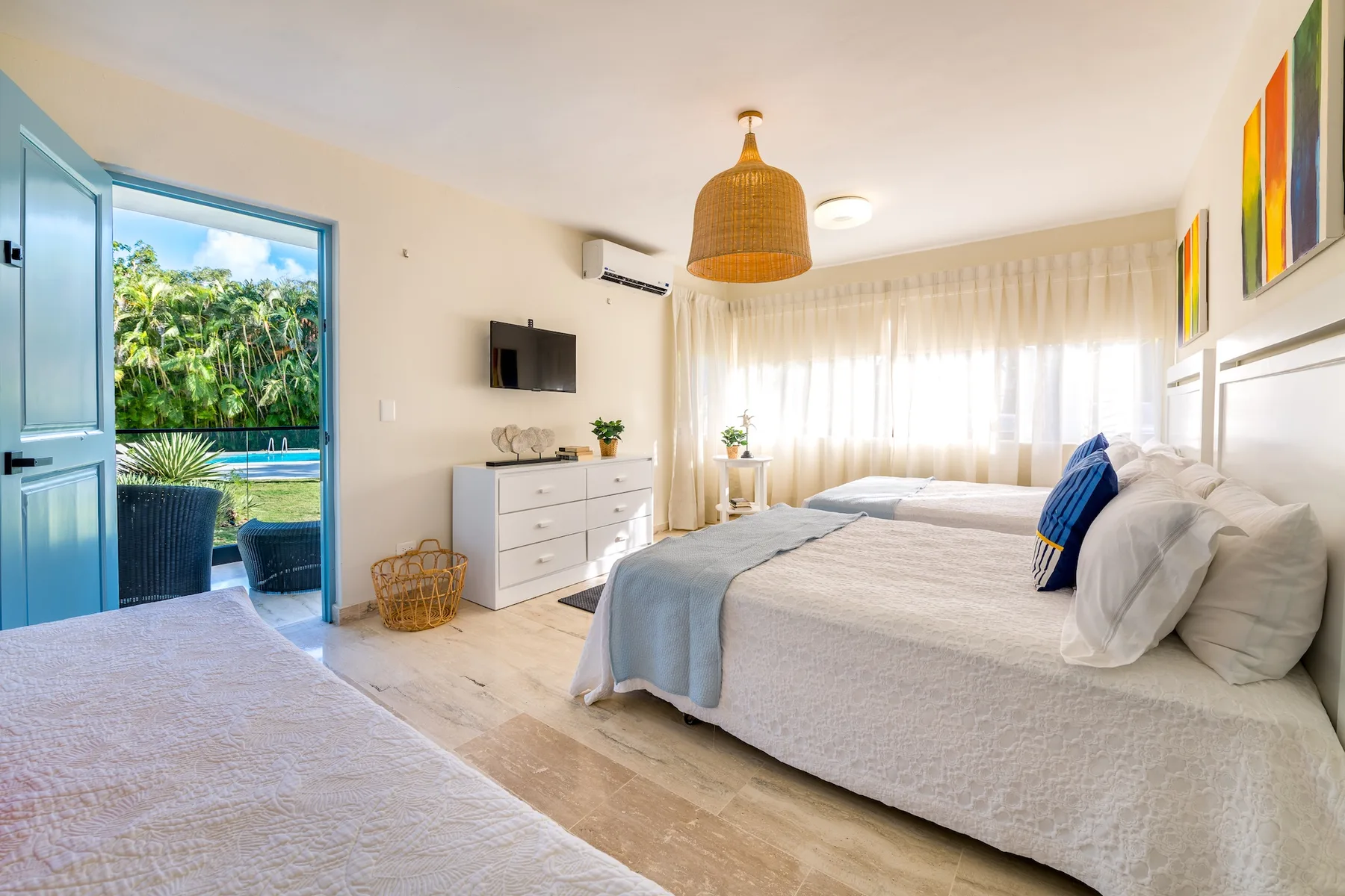 Un dormitorio luminoso con una cama grande, ropa de cama clara y una amplia ventana con cortinas.