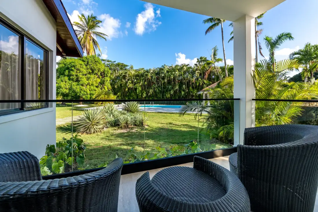 Un patio cubierto con asientos al aire libre da a un jardín y una piscina.