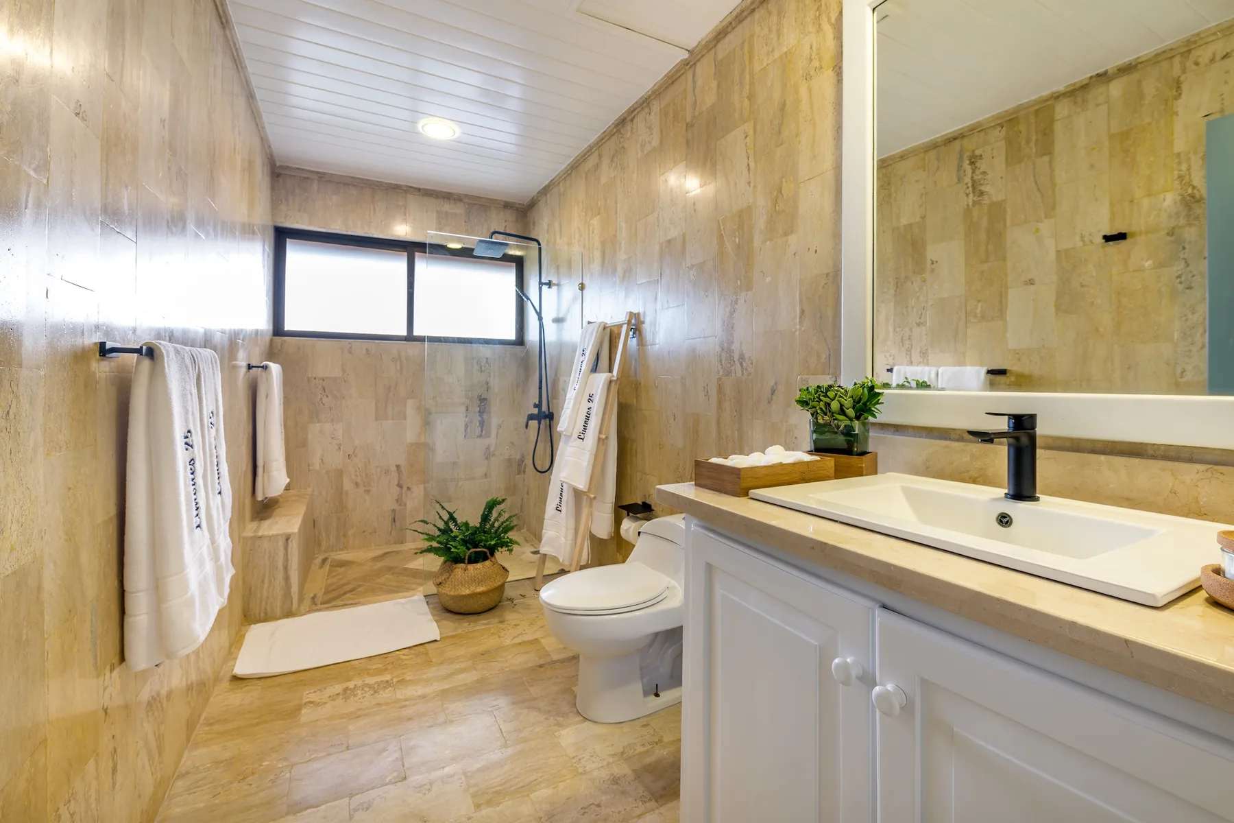 Un baño con bañera, inodoro y tocador bajo un espejo grande.