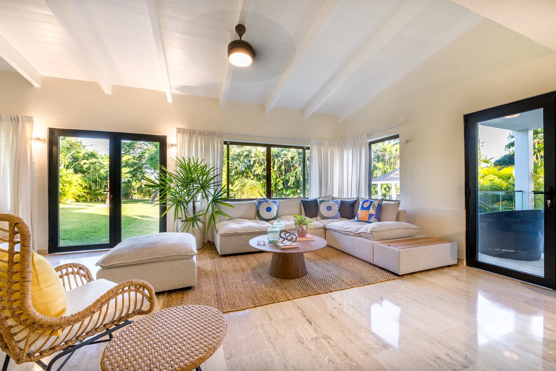 Una sala luminosa con asientos alrededor de una mesa baja y ventanas con vistas al jardín.