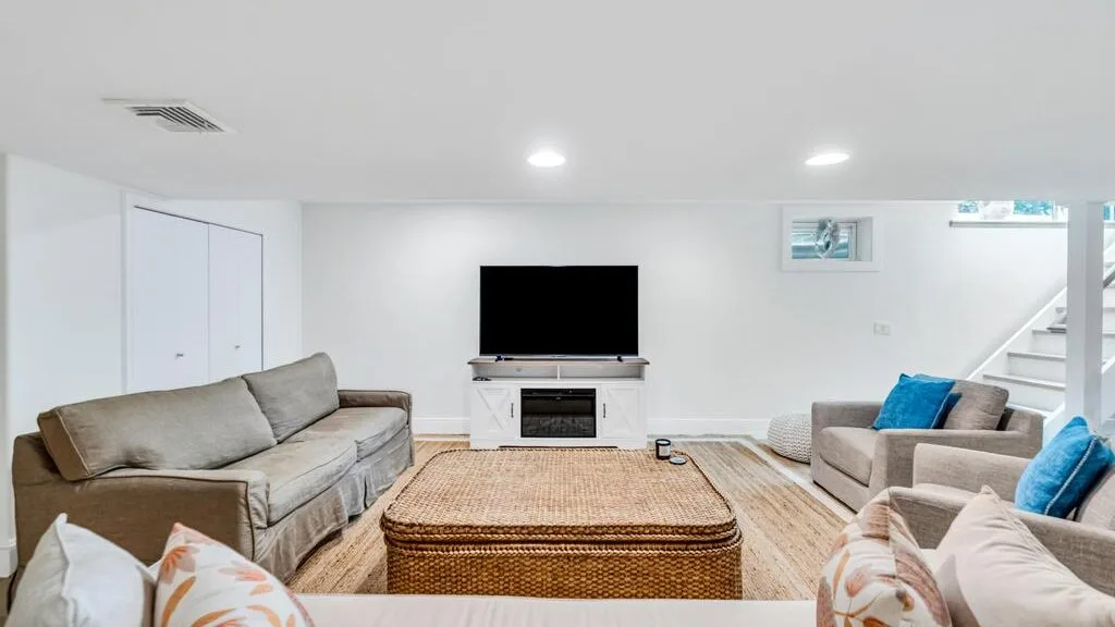 Una sala luminosa con sofás, una mesa de centro tejida y un televisor.
