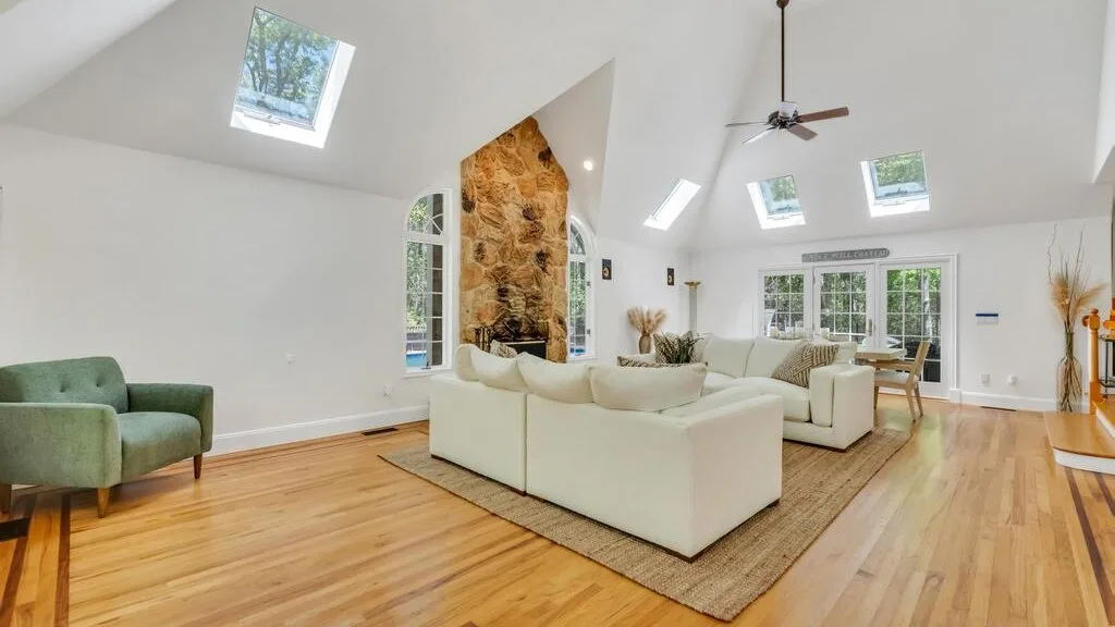Una luminosa sala de estar con asientos alrededor de una chimenea de piedra y grandes ventanas.