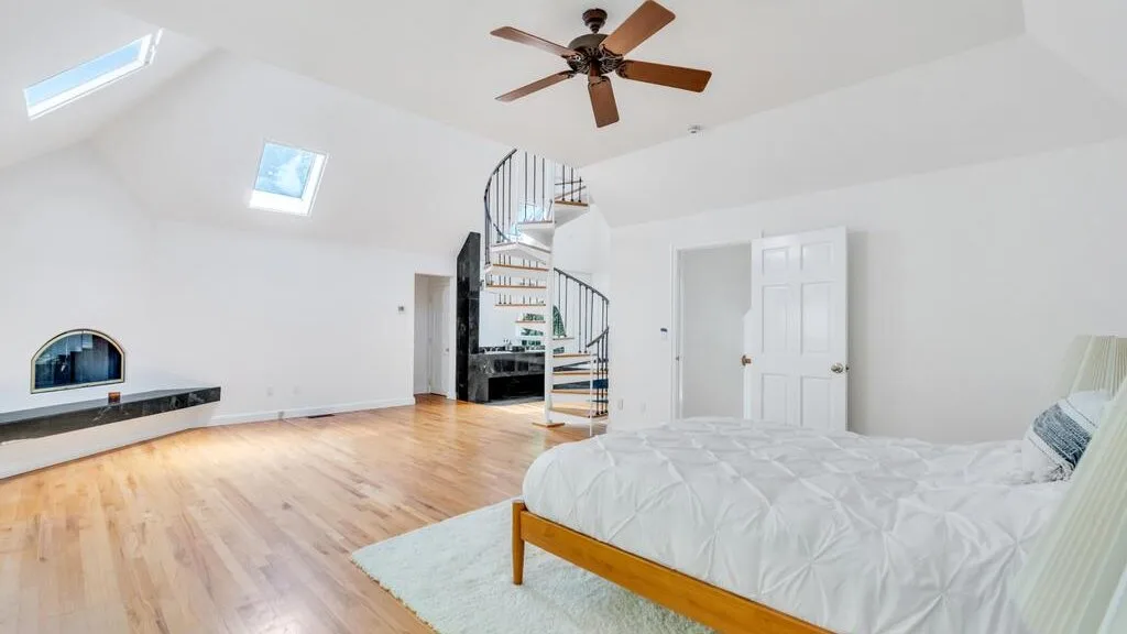 Un dormitorio luminoso con una cama, una escalera de caracol y techos inclinados.