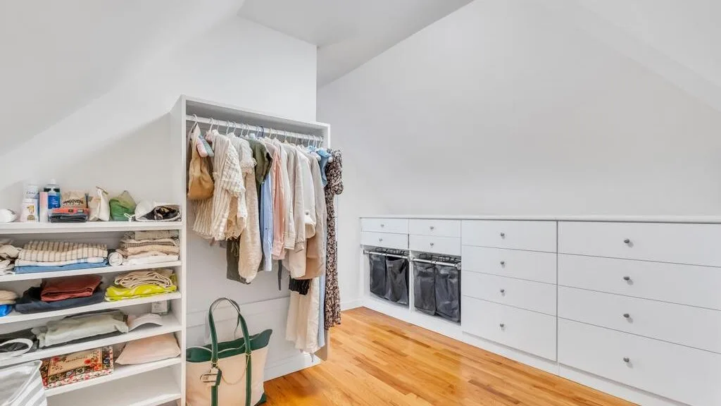 Un vestidor luminoso con ropa a la vista y cajones blancos.