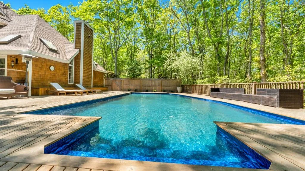 Una piscina al aire libre está junto a una terraza de madera, rodeada de árboles.