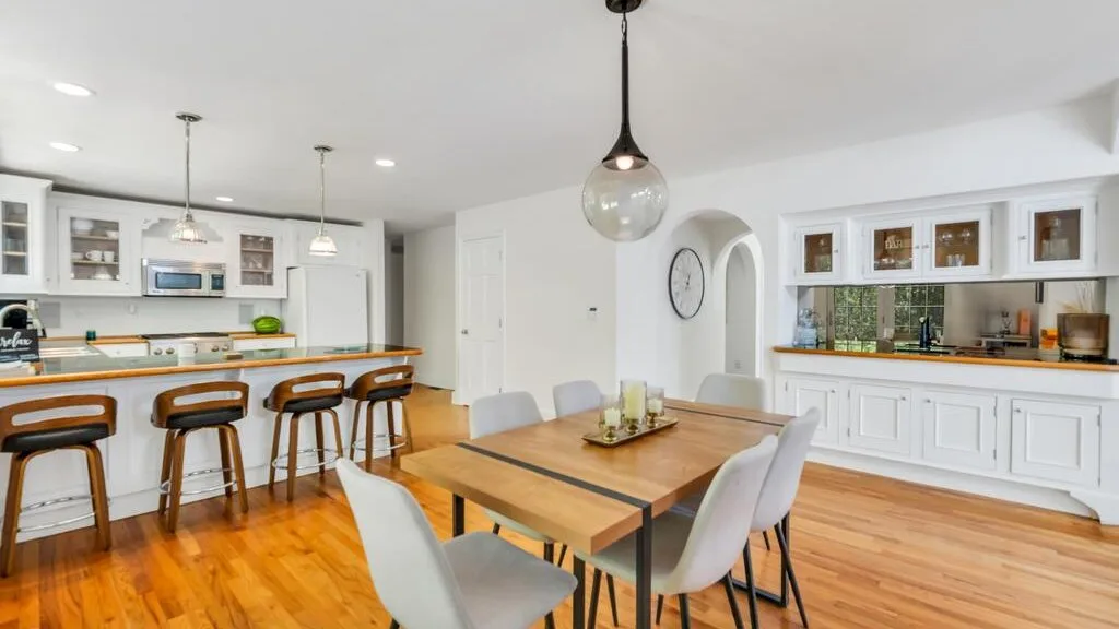 Una luminosa cocina-comedor de planta abierta con una mesa de madera y una barra.