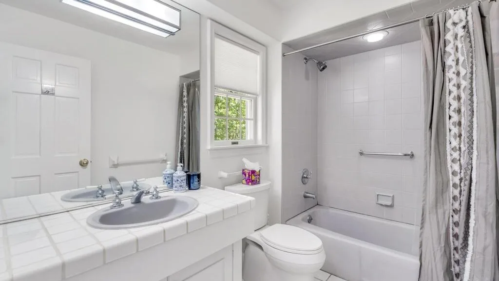 Un baño luminoso con lavabo de azulejos, inodoro y bañera detrás de una cortina de ducha.