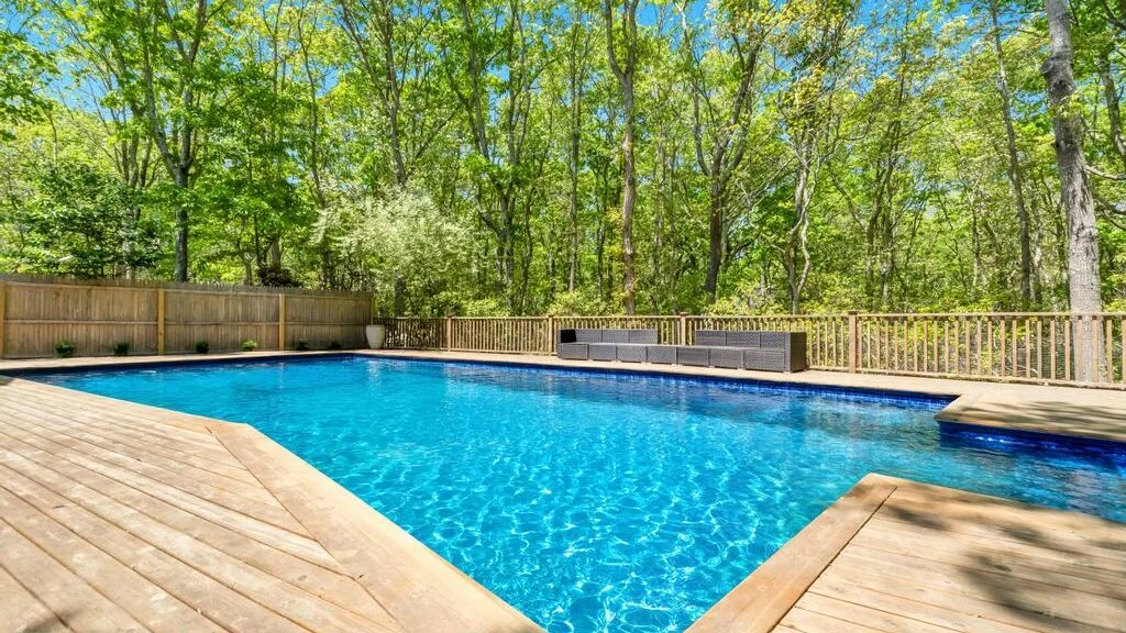 Una piscina al aire libre está rodeada por una terraza de madera y árboles.