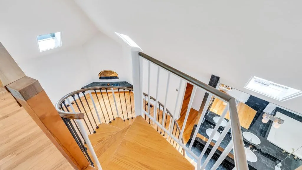 Una escalera con peldaños de madera y barandilla metálica da a un interior luminoso.