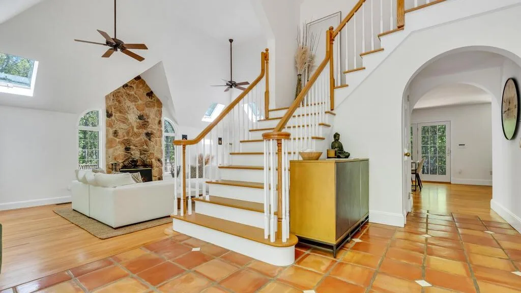 Una sala luminosa con una escalera y una chimenea de piedra.