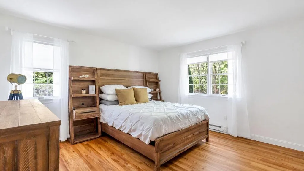 Un dormitorio luminoso con una cama de madera y dos ventanas.