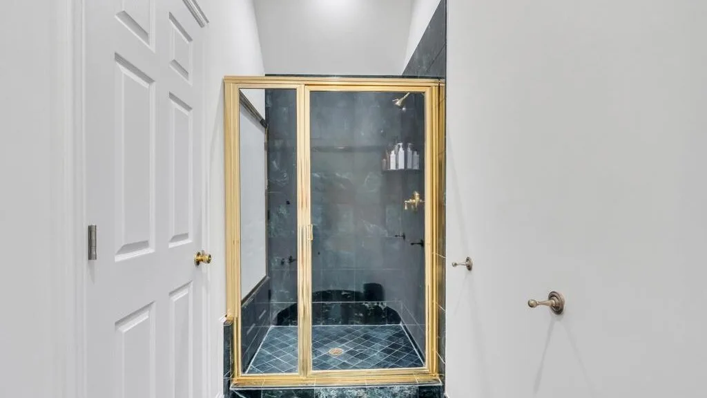 Un baño con una ducha de mampara de vidrio y paredes de azulejos oscuros.