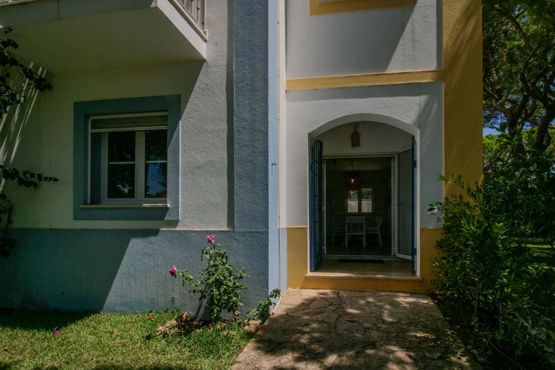A house entrance with an arched doorway, garden path, and surrounding greenery.