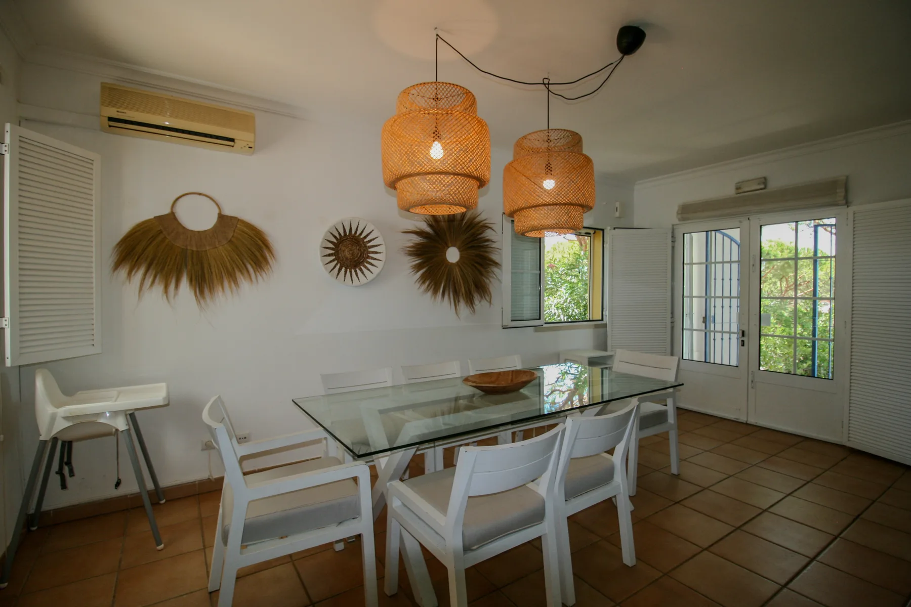 A dining area with a glass table and white seating beneath woven pendant lights.