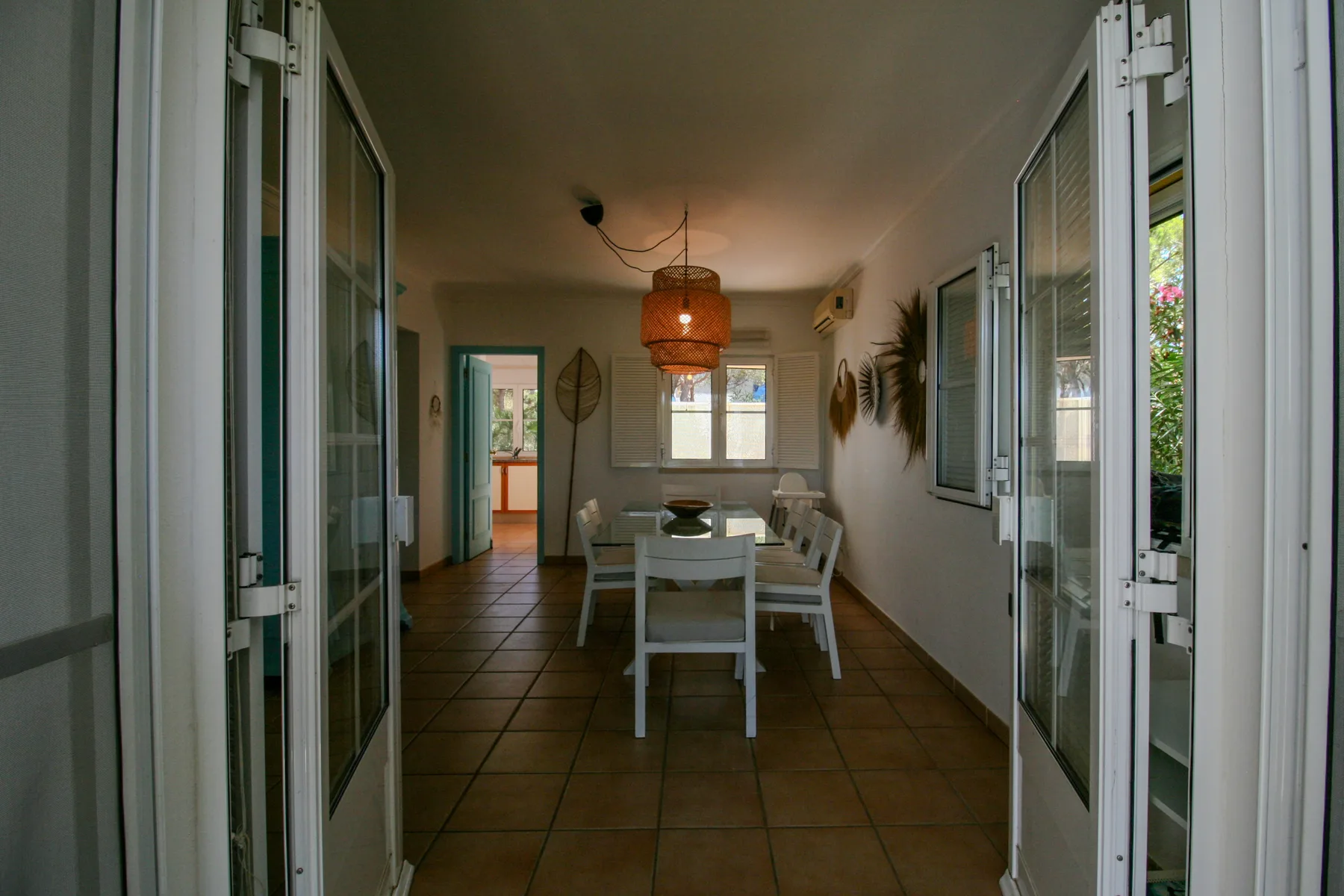 A dining area with a table and chairs sits between open glass doors.
