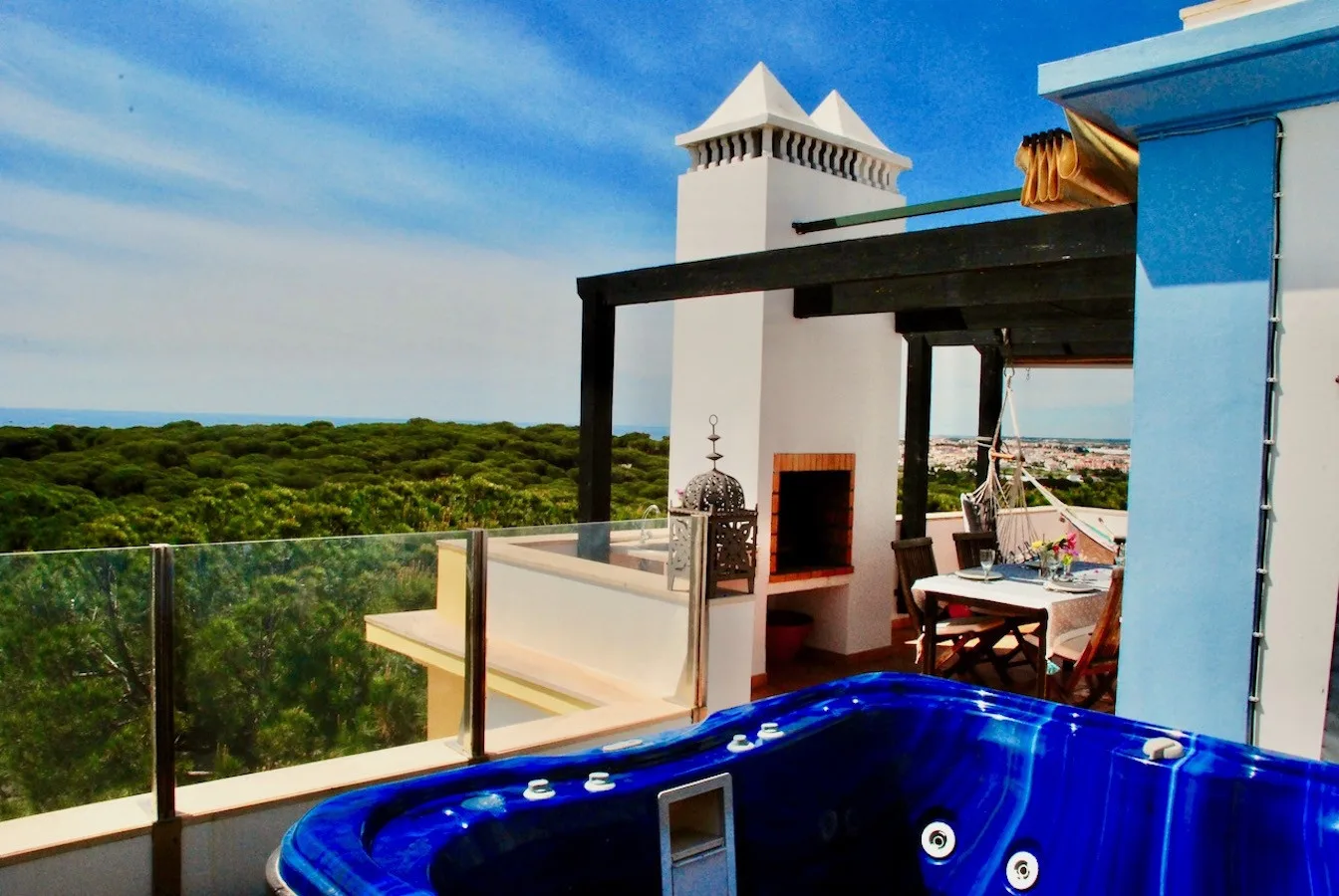 A rooftop terrace with a blue hot tub, glass railing, and outdoor seating.