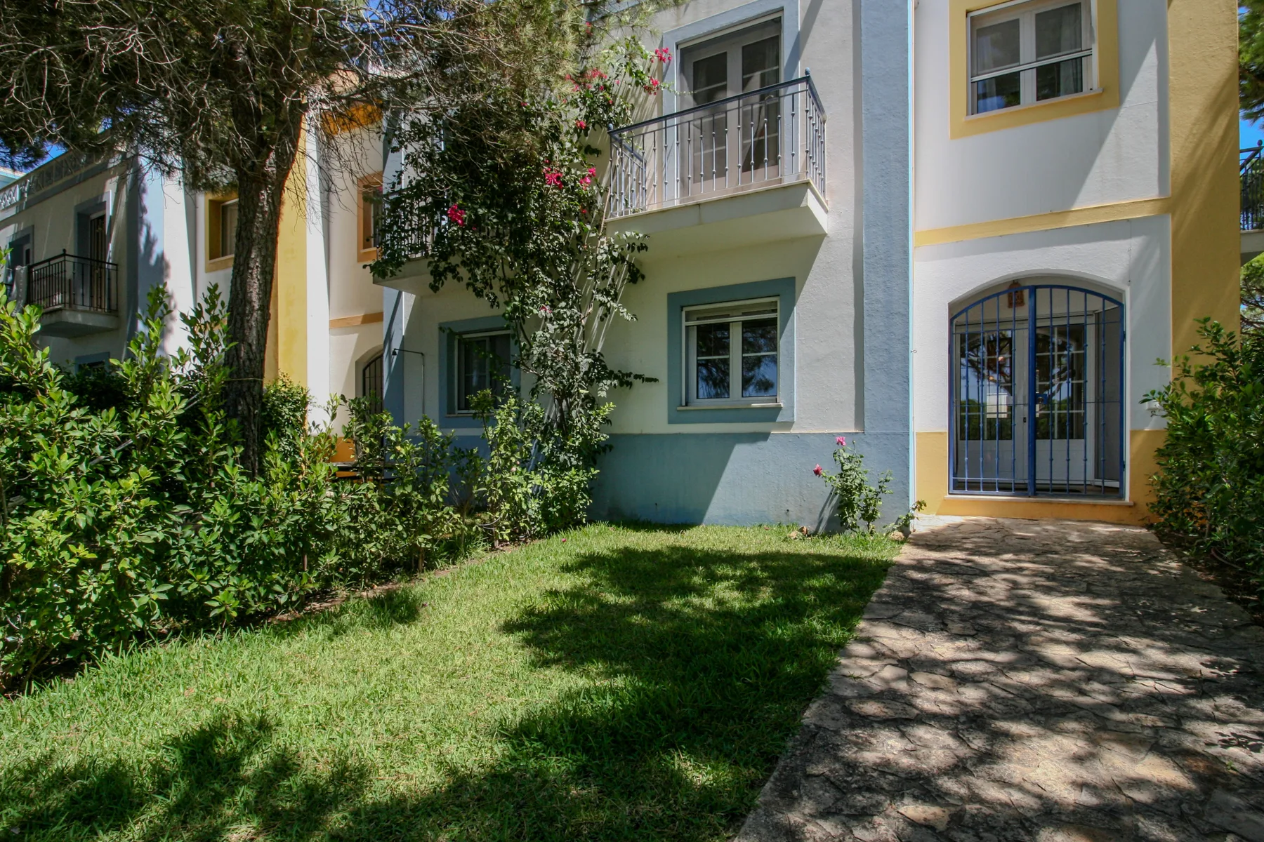 A pastel-colored house exterior with a garden and paved walkway.