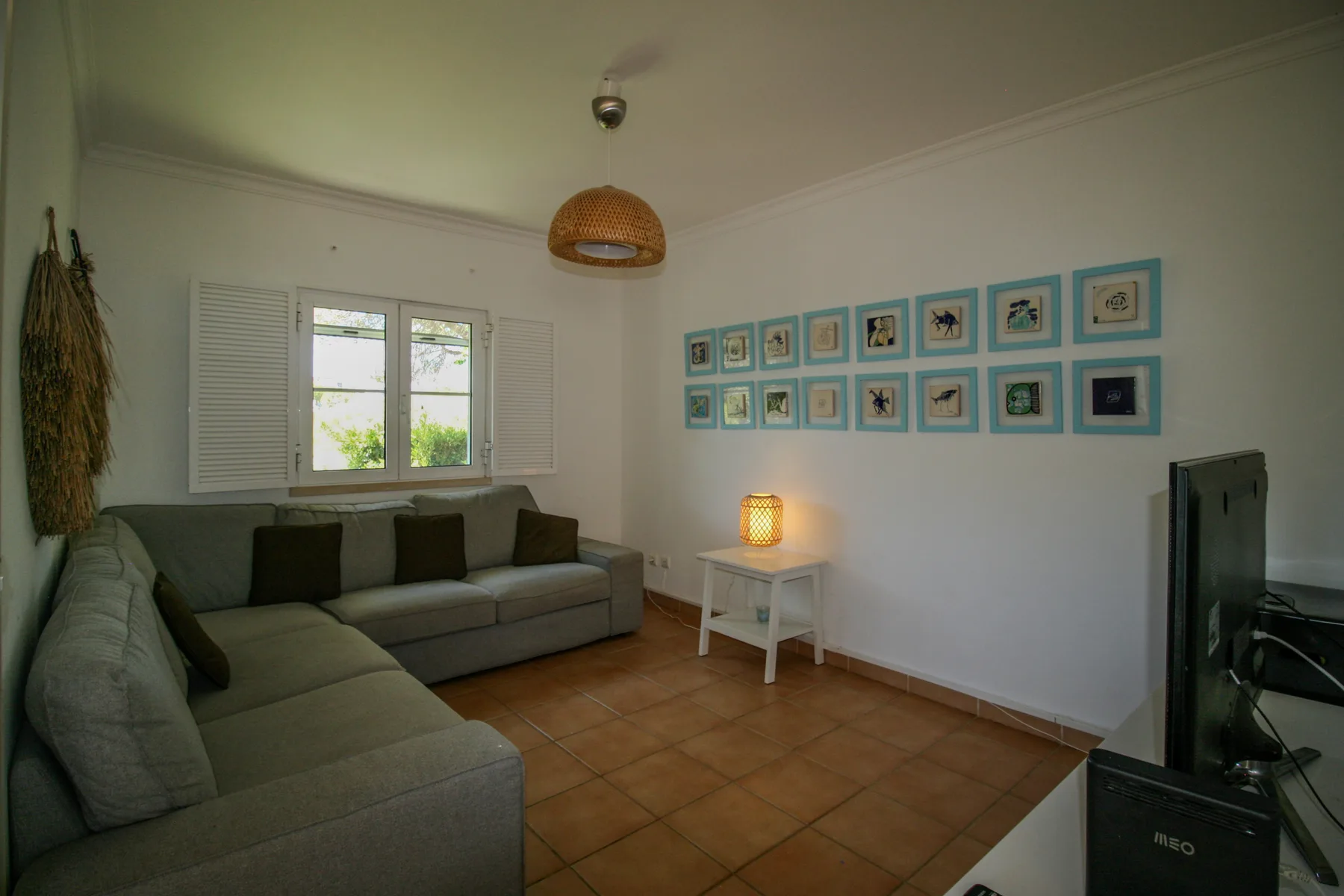 A living room with sectional seating, a window, and framed pictures on the wall.