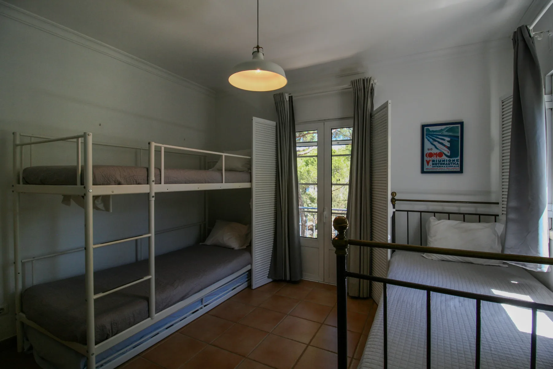 Un dormitorio con literas, otra cama y una puerta de cristal que da a un balcón.