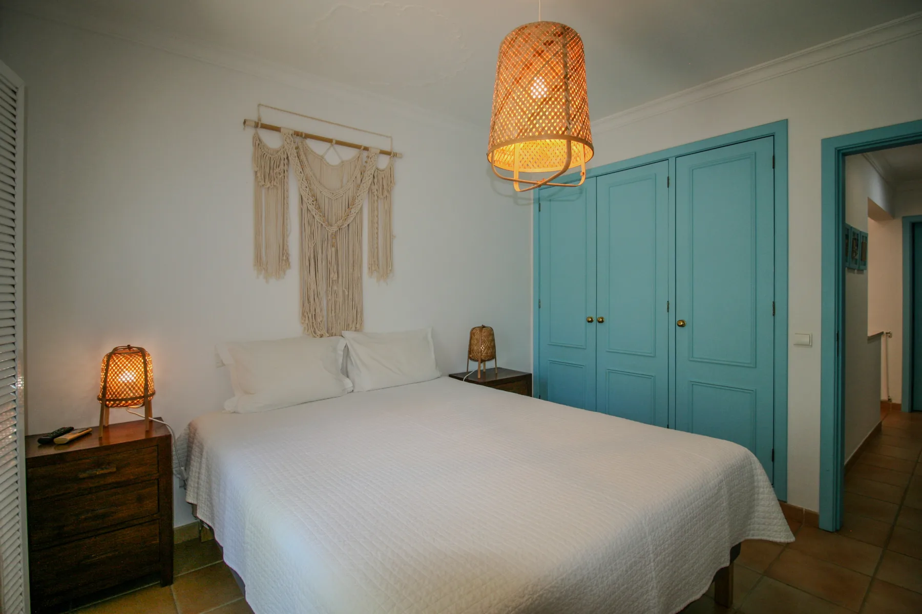 A bedroom with a double bed, turquoise wardrobes, and woven pendant lighting.