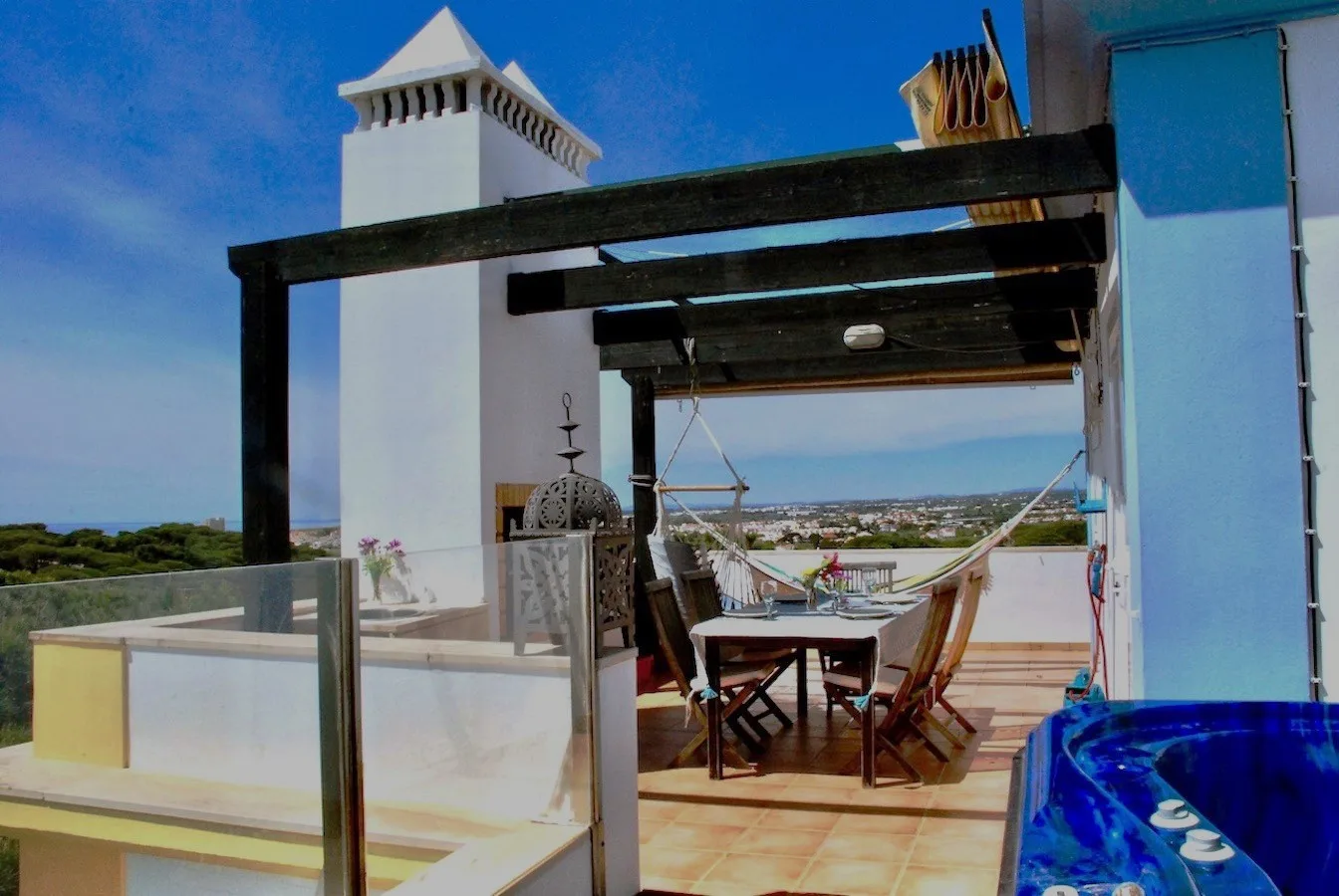 A rooftop terrace with a dining table, outdoor seating, and a view across the landscape.