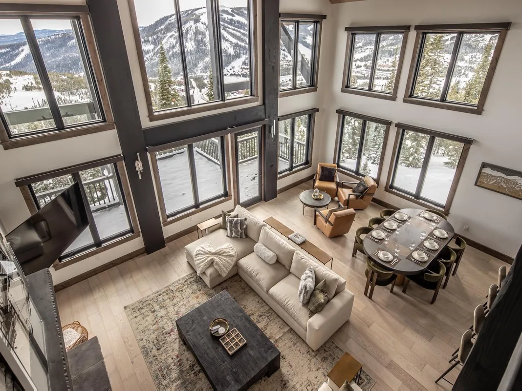 Una sala de estar y comedor de doble altura tiene grandes ventanas con vistas a un paisaje montañoso nevado.
