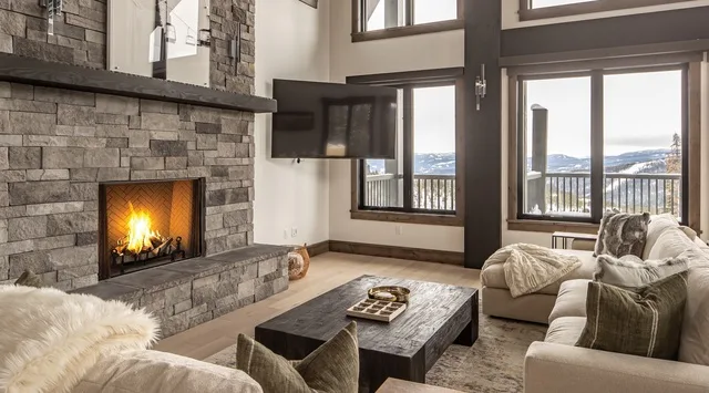 Una amplia sala de estar cuenta con una chimenea de piedra y grandes ventanas con vistas al paisaje.