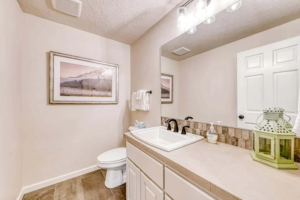 Un tocador de baño con lavabo y espejo junto a un inodoro.