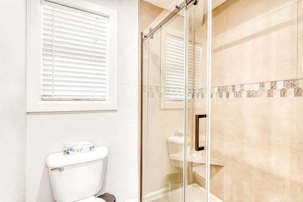 Baño luminoso con ducha de vidrio, inodoro y ventana.