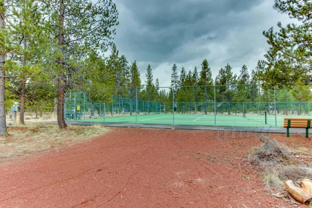 Una cancha de tenis al aire libre está rodeada de árboles altos bajo un cielo nublado.