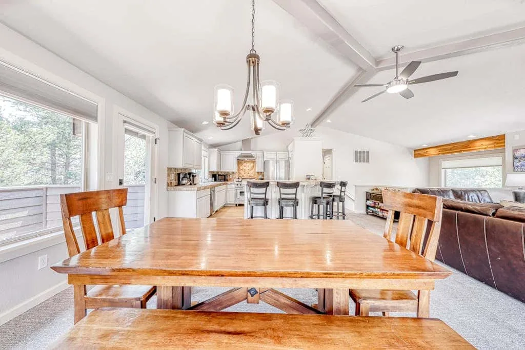 A bright dining area with a wooden table and an open kitchen beyond.
