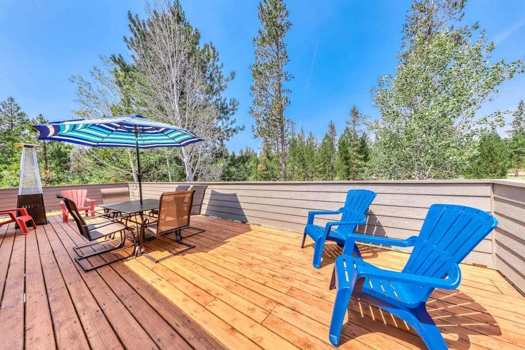Una terraza de madera tiene una sombrilla a rayas sobre una mesa y asientos azules.