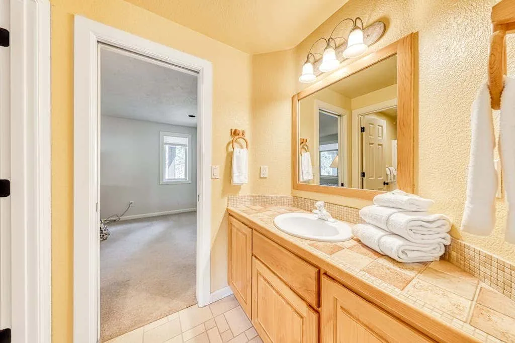 Un lavabo de baño con espejo, junto a una puerta abierta.