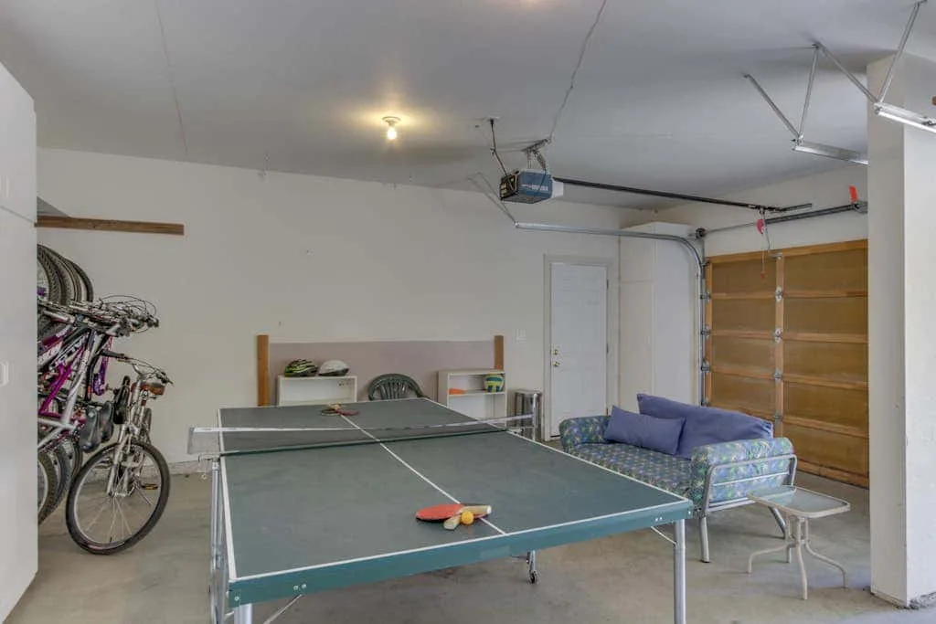 Una zona de juegos en un garaje con una mesa de ping-pong y asientos.