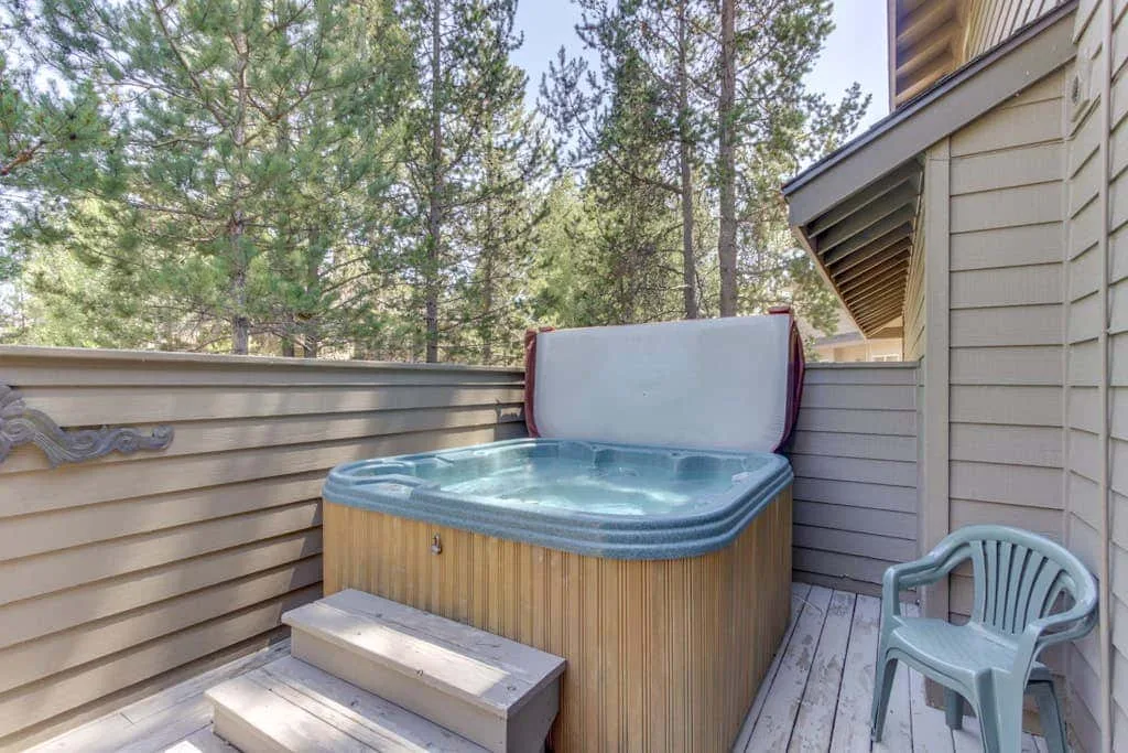 Una bañera de hidromasaje al aire libre está sobre una terraza de madera junto a una silla de plástico.