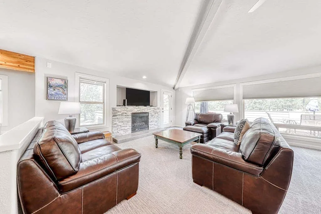 A bright living room with leather seating, a glass coffee table, and a fireplace.
