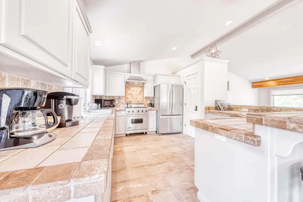 Una cocina luminosa con gabinetes blancos, electrodomésticos de acero inoxidable y encimeras de azulejos.