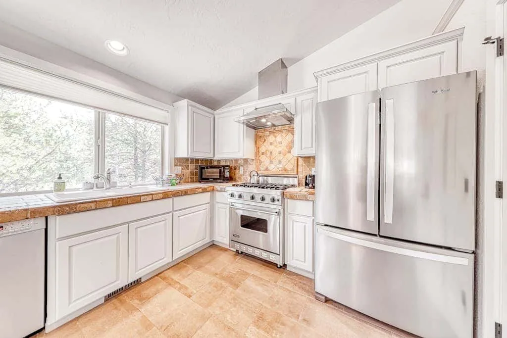 Una cocina luminosa con gabinetes blancos, un refrigerador de acero inoxidable y una ventana grande.