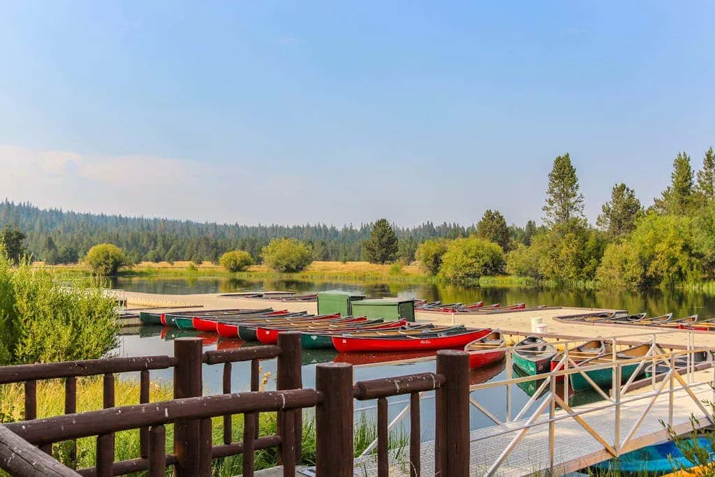 Un muelle junto al lago con canoas rojas, una barandilla de madera y árboles en la orilla.