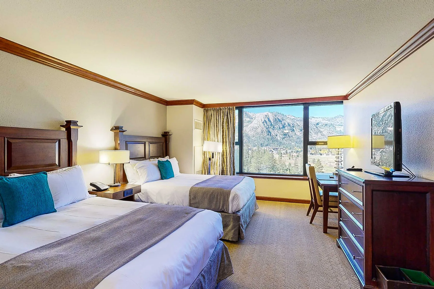 Un dormitorio con dos camas, un escritorio y una gran ventana con vistas a las montañas.
