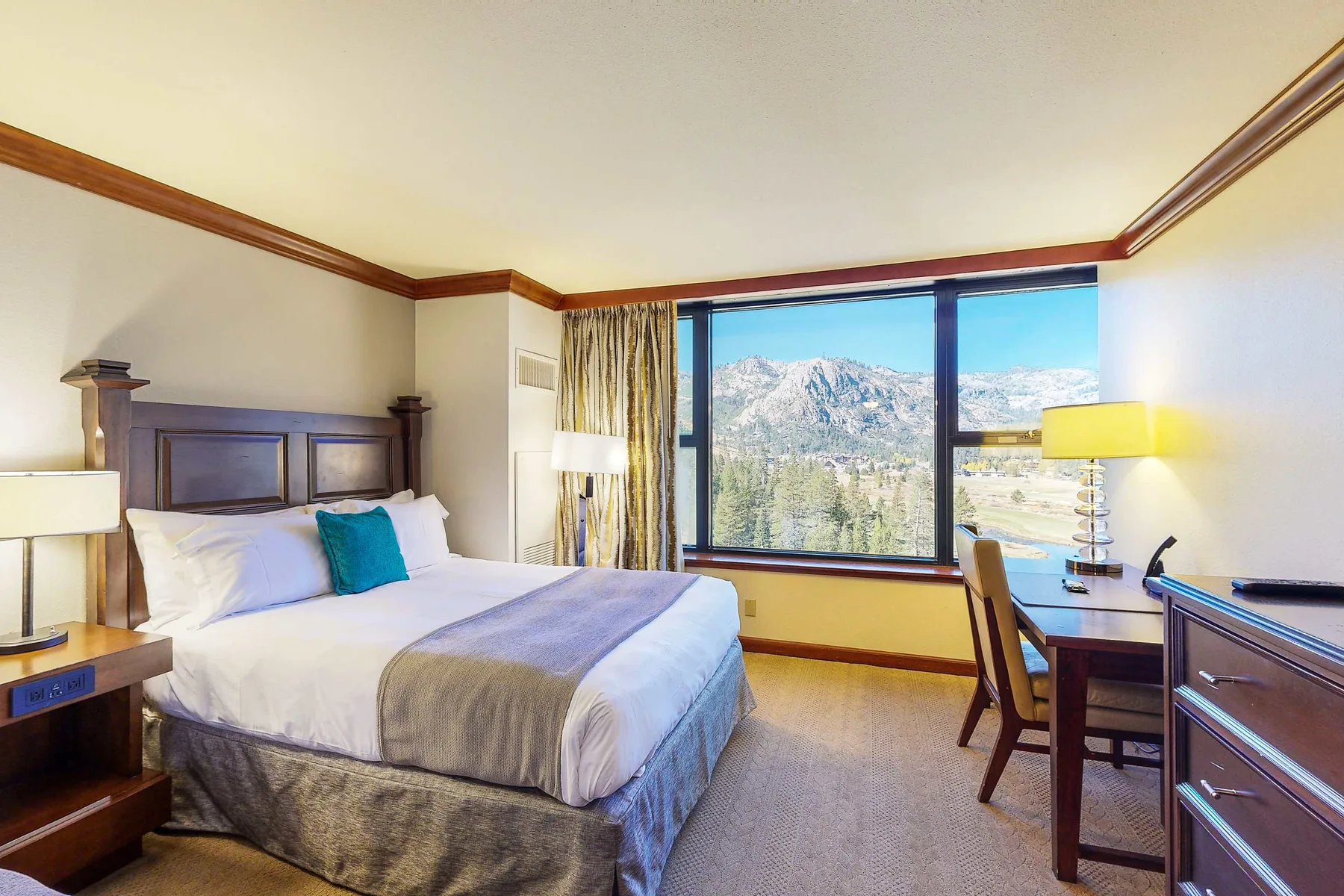 Un dormitorio con una cama, mesitas de noche y una gran ventana con vistas a las montañas.
