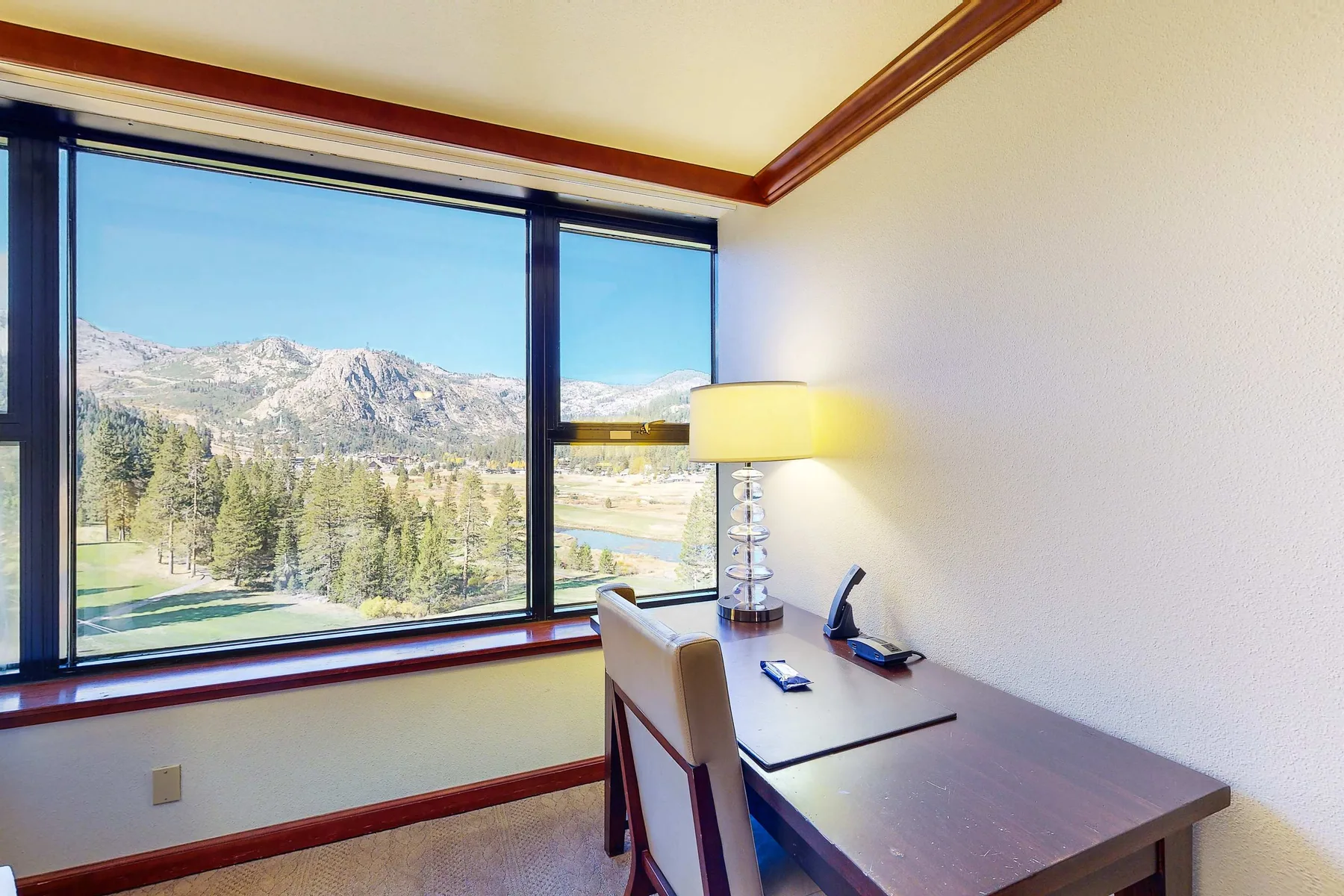 Un escritorio y una silla están junto a grandes ventanas con vistas a un paisaje montañoso.