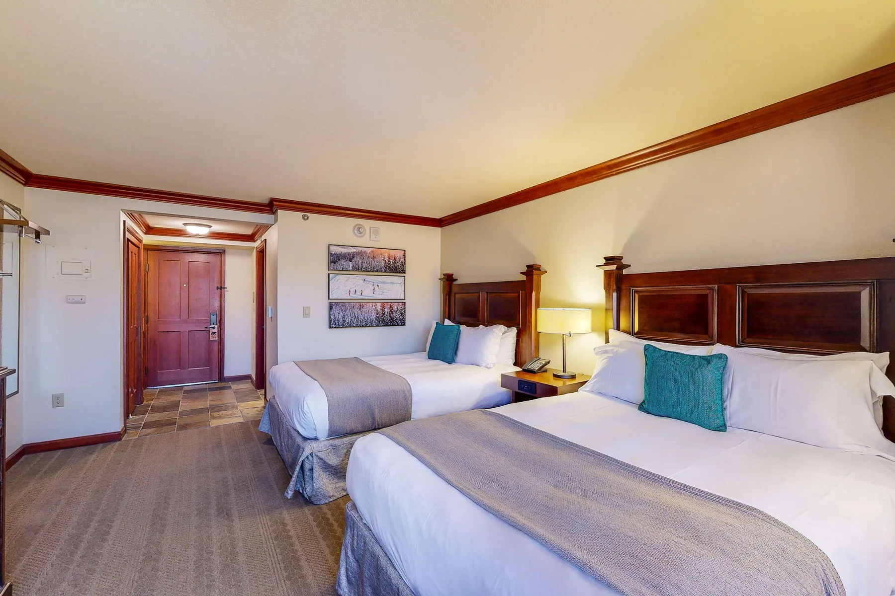 Un dormitorio con dos camas, cojines decorativos turquesa y cabeceros de madera oscura.