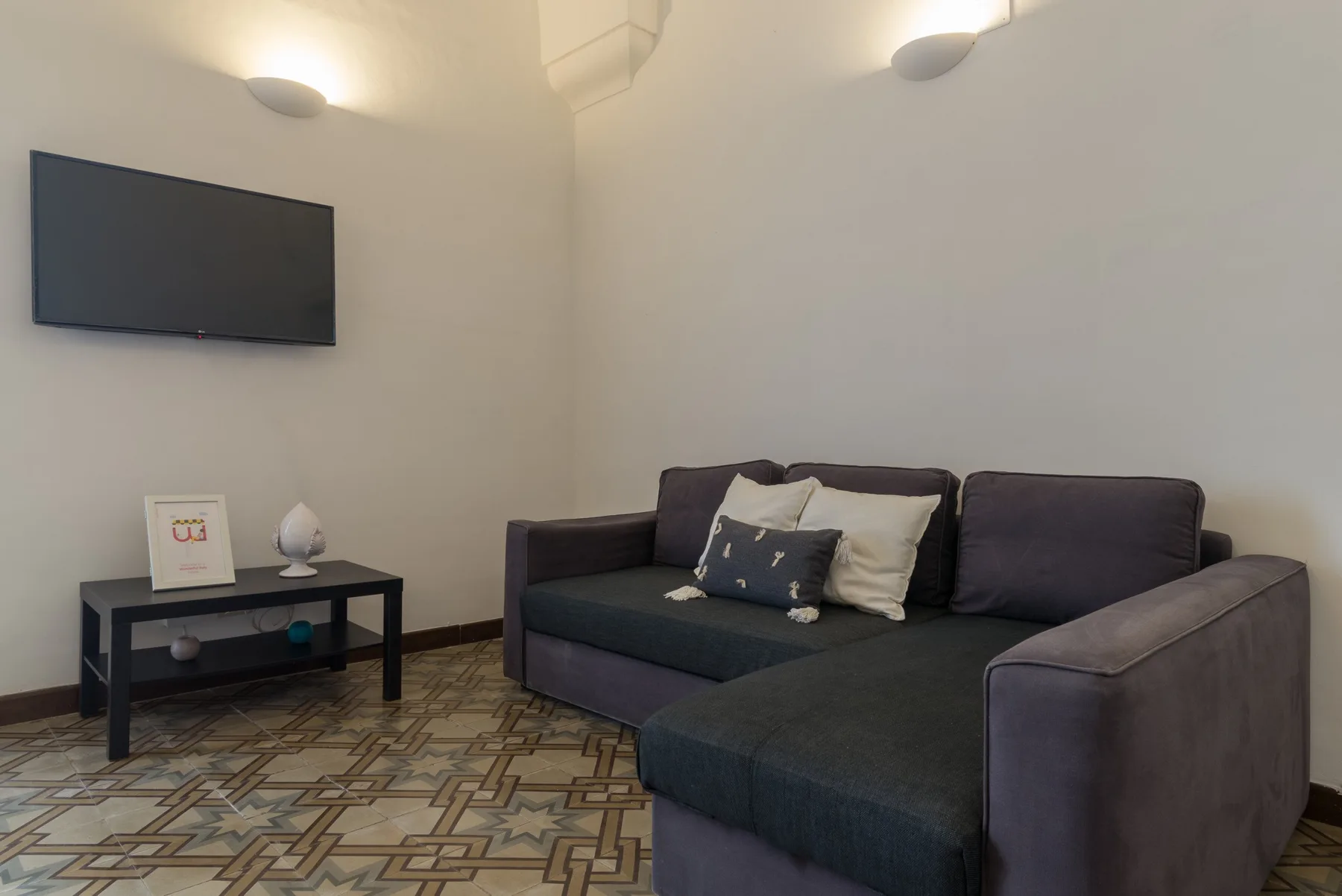 Una sala de estar con un sofá seccional oscuro y un televisor en la pared.