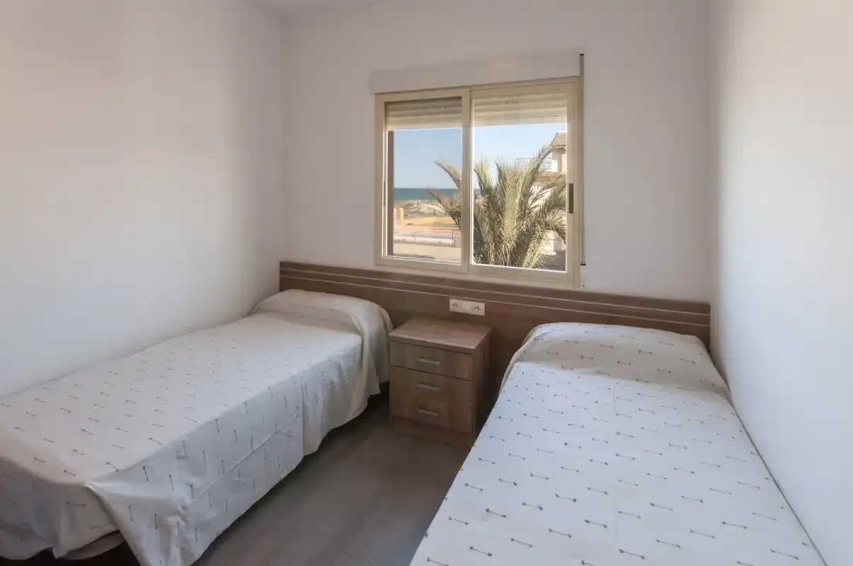 Un dormitorio con dos camas individuales y una mesita bajo la ventana.
