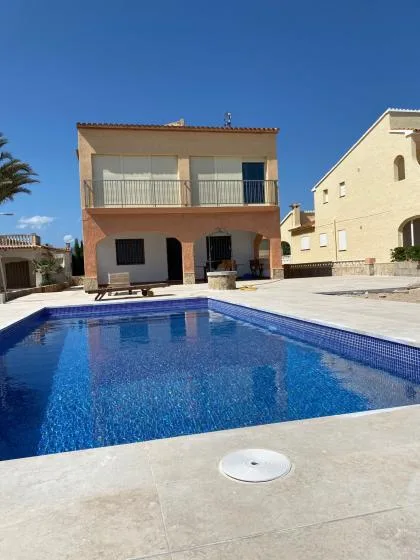 Una piscina está frente a una casa de dos plantas bajo un cielo azul despejado.